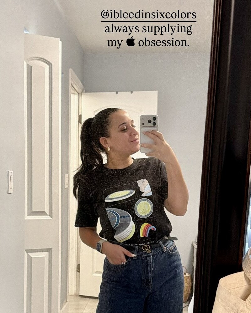 Woman taking a mirror selfie in the Apple Park Elements tee; her story text tags @ibleedinsixcolors