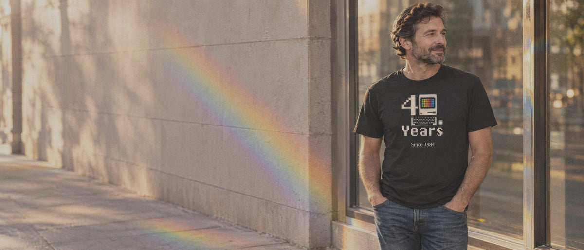 Man in a black Macintosh 40 Years tee on a sunlit sidewalk, a six-color light spectrum on the wall beside him